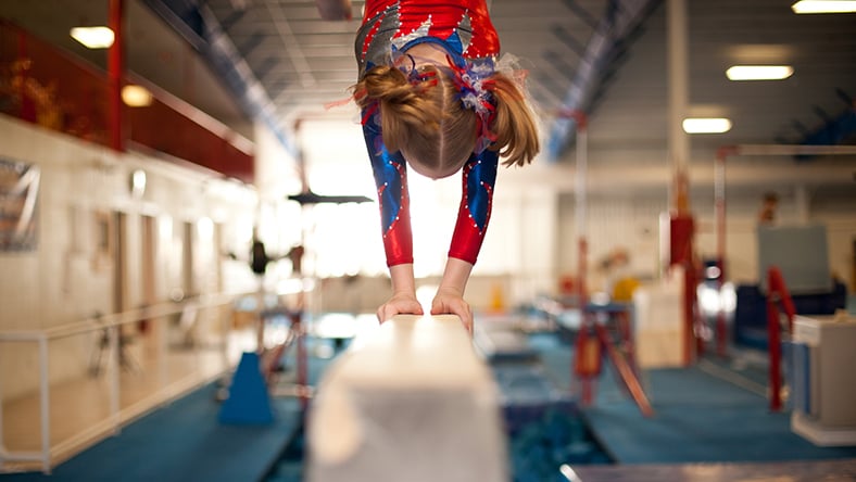 A young female gymnast doing a handstand on a balance beam