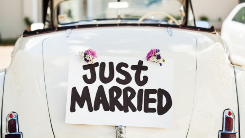 Just married sign attached to the back of a white vintage car with floral decorations.