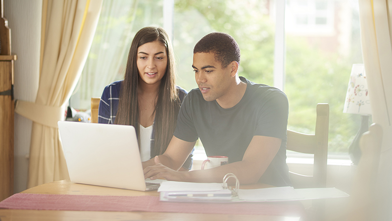 A young couple sitting at a table in front of a laptop