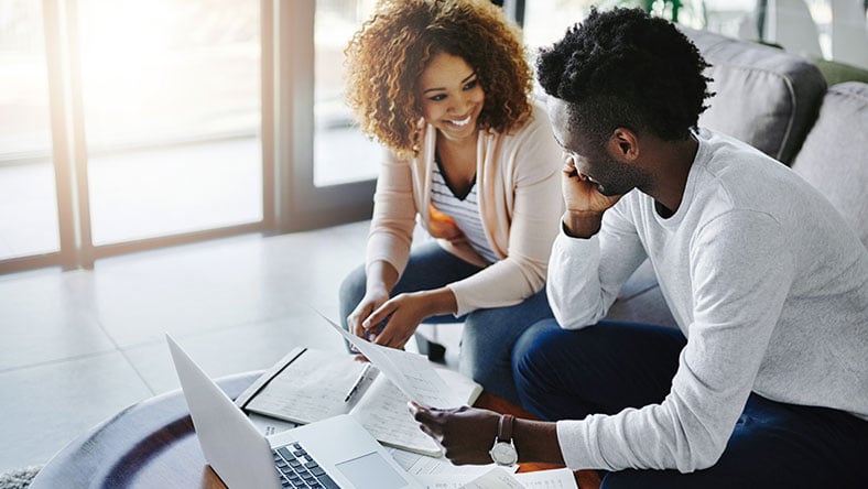 A couple reviewing documents while sitting on the couch in front of a laptop