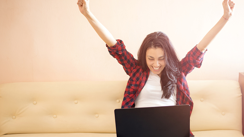 Woman raising her arms and smiling at her laptop
