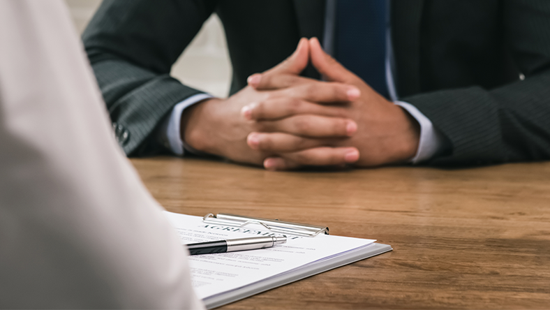 Man's hands folded on table with interview notepad