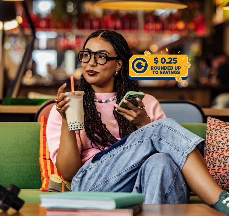 Person using a mobile phone with promotional graphic highlighting a $0.25 round-up to savings feature for checking account purchases.