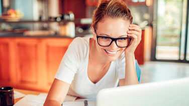Woman with glasses smiling while using laptop in kitchen