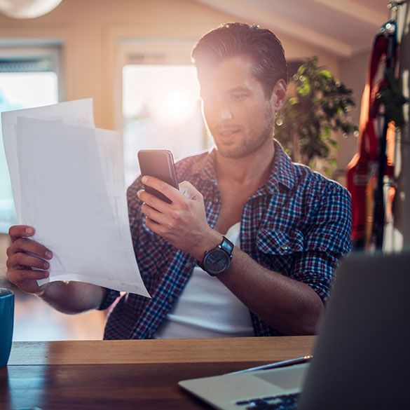 Young man sitting at home desk holding mobile device