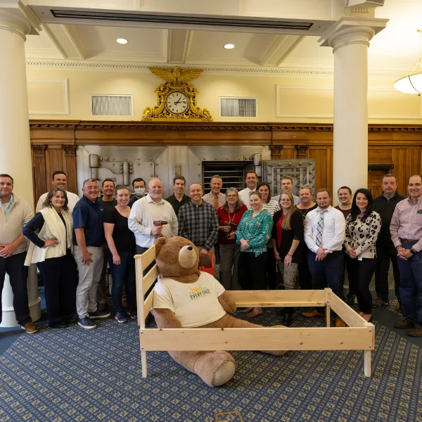 Salem Five team celebrating community involvement with group photo in bank lobby featuring vintage vault and teddy bear display.