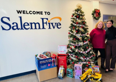 Salem Five employee standing next to Christmas tree and 2023 toy drive toys.