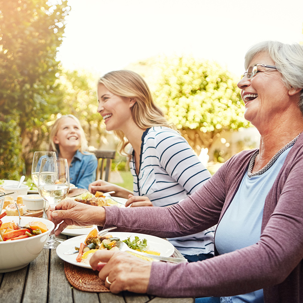 Smiling grandmother with family eating dinner on outside patio table.