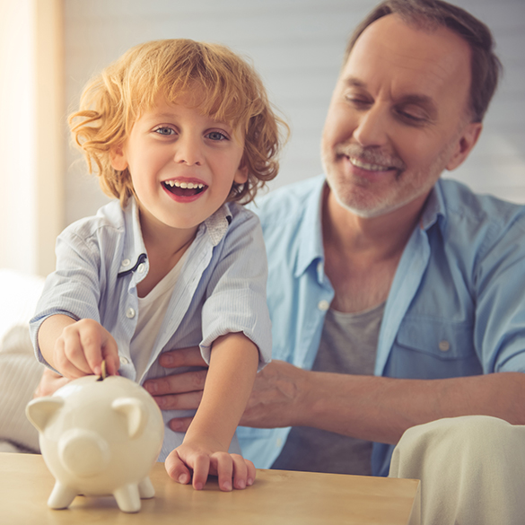 Happy dad watching young son put coin into a piggybank.