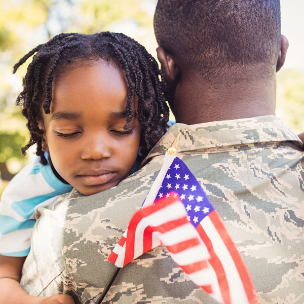 Veteran hugging young girl holding American flag.