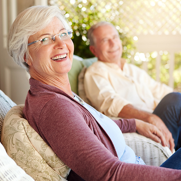 Mature couple smiling while sitting in a sunroom.