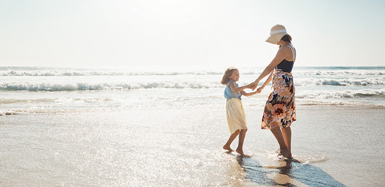 Woman and child holding hand by the water at the beach